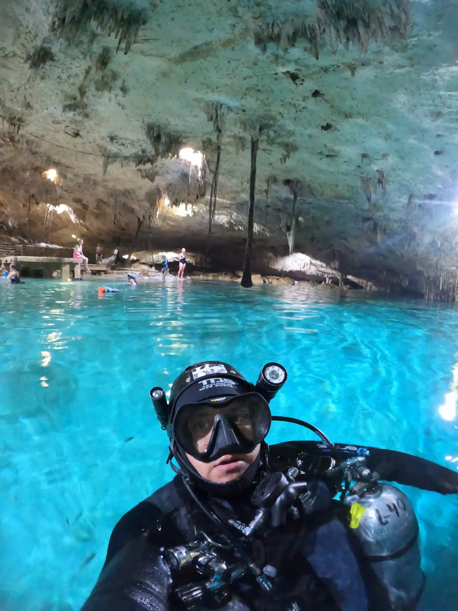 Buceador en caverna subacuática iluminada por haces de luz natural con formaciones rocosas y visibilidad cristalina<br />
