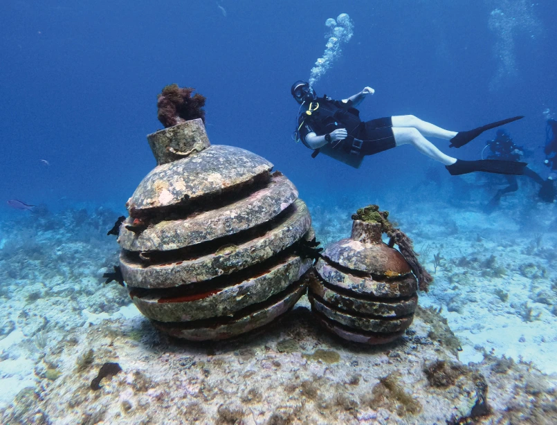 Buceador en caverna subacuática iluminada por haces de luz natural con formaciones rocosas y visibilidad cristalina<br />
