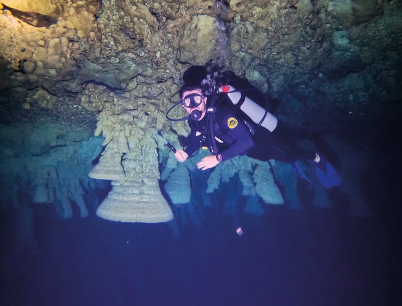 Buceador en caverna subacuática iluminada por haces de luz natural con formaciones rocosas y visibilidad cristalina<br />
