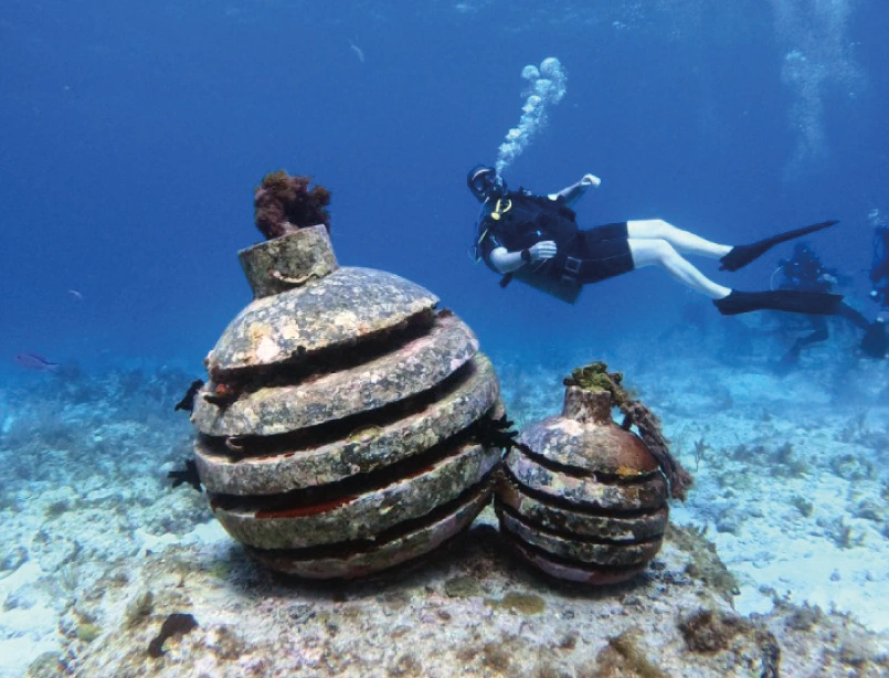 Buceador en caverna subacuática iluminada por haces de luz natural con formaciones rocosas y visibilidad cristalina<br />
