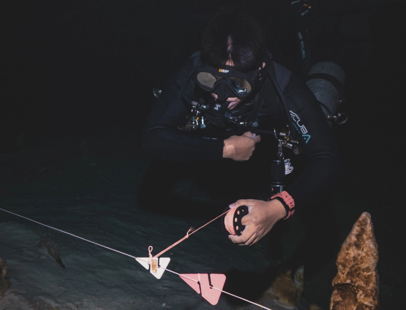 Buceador de caverna en cenote usando un carrete de línea guía durante una inmersión guiada cerca de Cancún